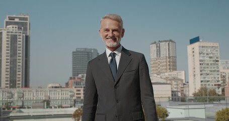 Fototapeta premium Smiling businessman standing outdoors against cityscape, enjoying professional success