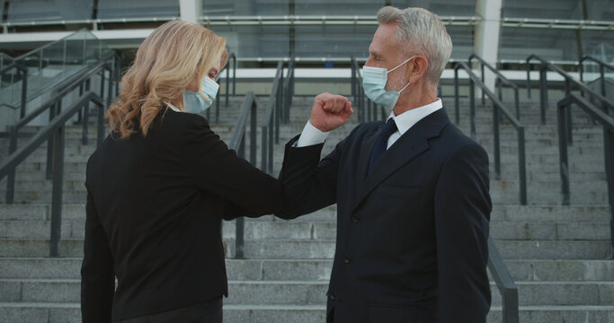 Male and female colleagues in protective masks doing elbow bump, epidemic safety measure