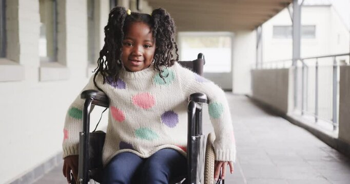Smiling girl in wheelchair enjoying school hallway, wearing colorful sweater