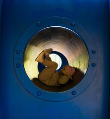 A girl dressed in casual clothes and a pink cap happily slides through a blue tunnel on a playground, enjoying a fun day in the warm sun. Child playing in tunnels on a playground.