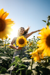 Young woman holding a sunflower on the sunflower field with blue sky.