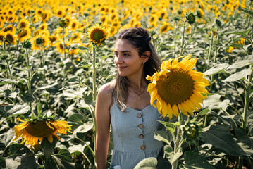 Young woman holding a sunflower on the sunflower field with blue sky.