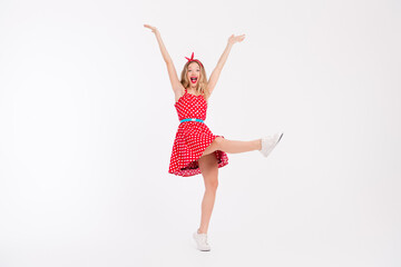 Fototapeta na wymiar Energetic young woman in vintage polka dot dress expressing joy and freedom on white background, showcasing retro fashion and dance moves.