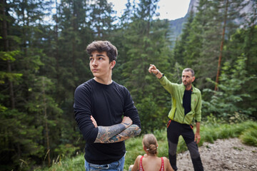 Young man and guide exploring a forest trail in the mountains during sunny summer day
