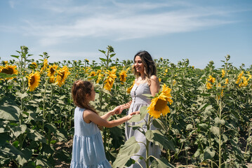 Mother and her little daughter standing in sunflower field.