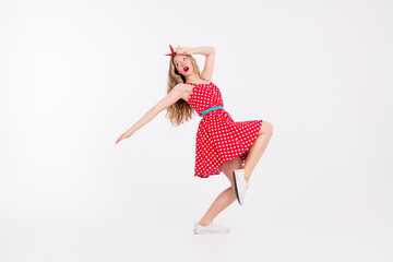 Young blonde woman in a red polka dot dress dancing gracefully against a white background, evoking fun