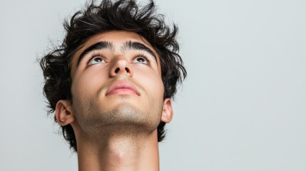 Fototapeta premium Thoughtful Young Man Looking Upward Against a Light Background, Pensive Expression