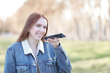 Long-haired woman walks through a park dictating on her mobile phone