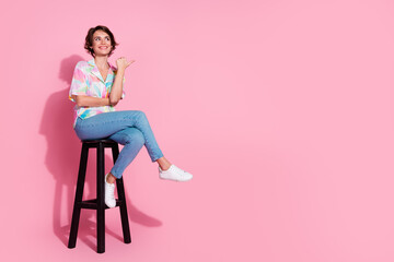 Full body portrait of nice young woman sit stool point finger empty space wear shirt isolated on...