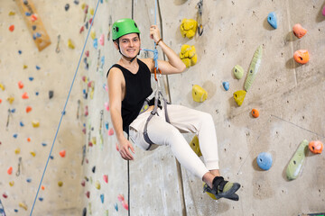 male climber in helmet and with safety rope hangs near climbing wall in gym. dynamic sports