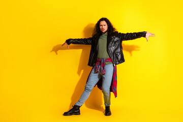 Young man in leather jacket posing on yellow background with stylish outfit and expressive gesture in trendy fashion