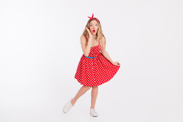 Cheerful young lady in a vintage red polka dot dress posing playfully against a white background