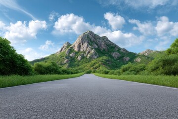 A long grey road leads to a rugged green mountain under a partly cloudy blue sky
