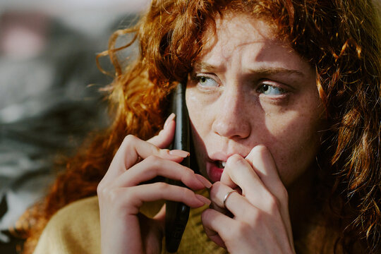 Woman having serious conversation on mobile phone, with red hair, outdoors in natural light. Her expression appearing concerned and focused