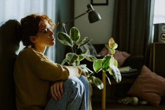 Woman in casual clothes sitting on floor, leaning on wall and immersed intro thoughts