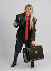 Standing confidently in a trench coat and red tie, the woman holds sunglasses and a briefcase, with...