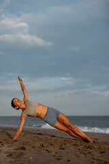 Female Athlete Performing a Side Plank Yoga Pose on a Beach at Sunrise