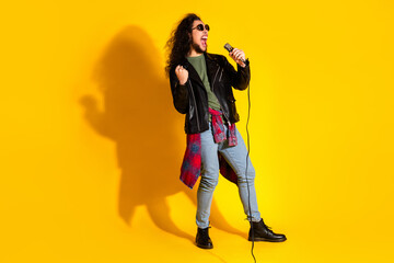 Stylish young man with a microphone passionately singing in a pose against a vibrant yellow background