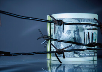 Economic warfare and sanctions concept. US Dollar bills money wrapped in barbed wire. Copy space...