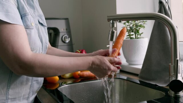 washing fresh carrots under running faucet in