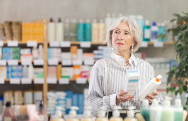 Elderly female pensioner in summer clothes choosing skin cream at the drugstore