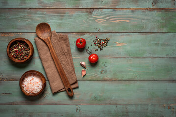 Wooden spoon, linen napkin, pink salt, peppercorns, tomato and garlic on old wooden table, top view, flat lay
