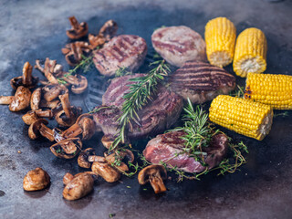 Rib eye and filet mignon steaks with corn and mushrooms on the grill.	
