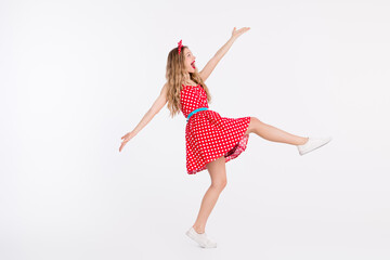 Young woman in a retro polka dot dress dancing joyfully against a white background, stylishly showcasing vintage charm and cheerful energy