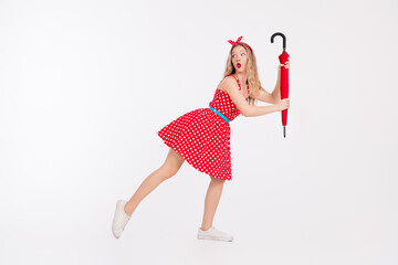 Retro styled woman in polka dot dress holding a red umbrella in a dynamic pose on a white background