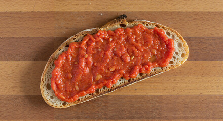 Slice of bread topped with red tomato sauce on wooden board  