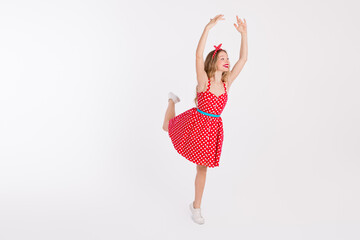 Young woman in red polka dot dress dancing energetically with joyful expression against white...