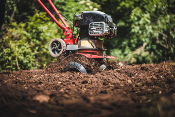 Close up photo of gardener cultivate ground soil rototiller , tiller tractor, cutivator, miiling machine, prepare for planting crop, spring. modern farming, technology agriculture.