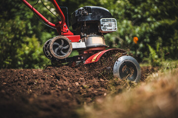Close up photo of gardener cultivate ground soil rototiller , tiller tractor, cutivator, miiling machine, prepare for planting crop, spring. modern farming, technology agriculture.