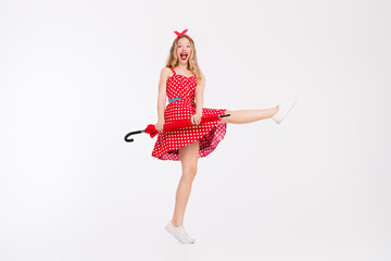 Young woman in retro red polka dot dress holding umbrella, posing joyfully against a white background