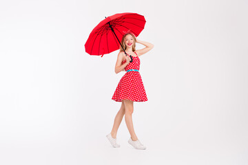 Young blonde girl in a red polka dot dress holding a red umbrella against a white background...