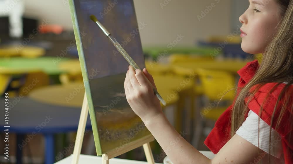 Aufkleber a focused girl is painting a landscape with a brush on a canvas propped on a wooden easel. the class