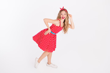 Smiling young woman in retro red polka dot dress posing playfully against a white background, expressing happiness