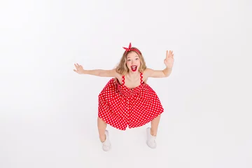 Gordijnen Young woman in a red polka dot dress dancing energetically against a white background, showcasing a vintage retro style © deagreez
