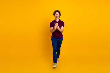 Young man holding a smartphone in front of a yellow background showcasing his casual and stylish appearance