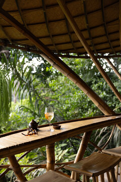 Cocktail with ice in a wine glass served with a dish of peanuts next to tortoise shell sunglasses with view of rice paddies in an open-air structure in Bali, Indonesia. 