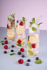 three refreshing infused water glasses adorned with lemon slices, raspberries, blueberries, and mint leaves, on a light blue surface creating a vibrant and invigorating summer setting, refreshment