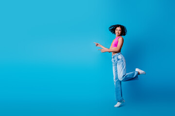 Joyful young woman in vibrant casual outfit posing against blue background in playful and energetic movement