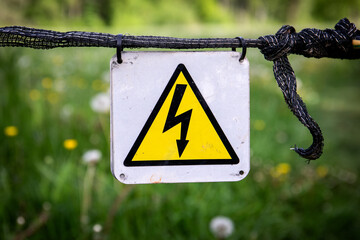 Warning Sign for Electrical Hazard Mounted on Fence with Green Field Background
