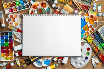 Obraz premium Watercolor paint in old used plastic palettes, creative mess. Album notebook with white sheets for painting. Copy space, empty blank, mock up