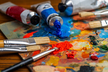 Old used brushes and paint tubes in an artist's studio, palette with multi-colored spots of oil or...