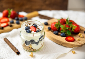 White yogurt in glass bowl with blueberries and strawberries and oatmeal on white background.