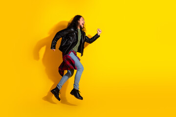 Energetic young man leaping with joy in a leather jacket against a vibrant yellow background,...