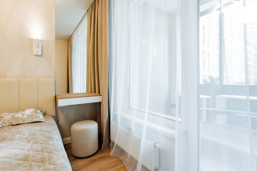 The spacious bedroom features a comfortable bed, a stylish ottoman, an elegant mirror, and a large window that lets in plenty of natural light. This creates a bright and inviting atmosphere