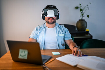 Man Wearing Virtual Reality Headset Indoors While Working at Desk with Laptop and Documents Highlighting Technology's Role in Everyday Tasks