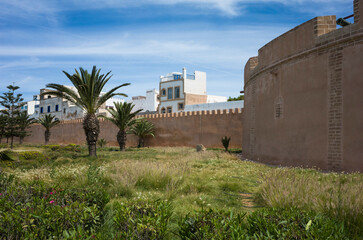 Old city wall of Essaouira, Morocco, with palm trees, grass, and traditional white buildings in the...